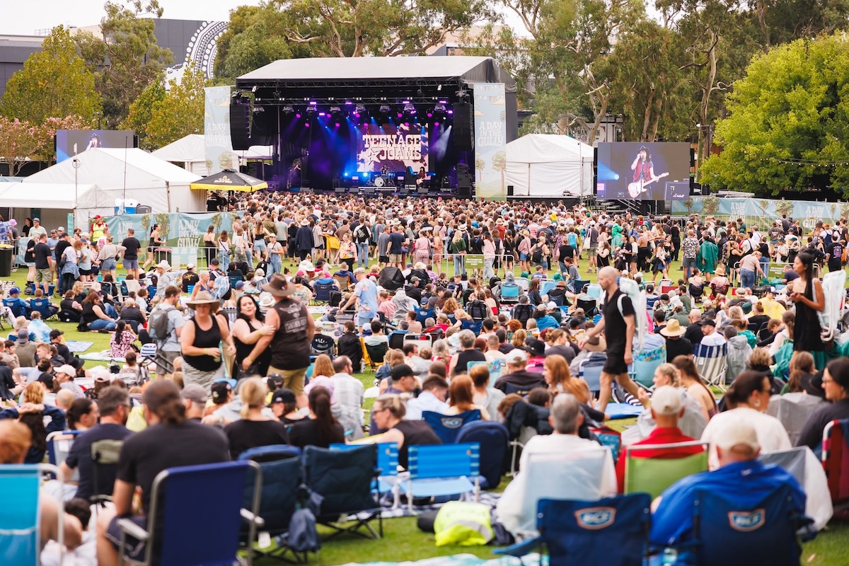Large crowd enjoying an outdoor music festival with a stage and screens at A Day in the Gully.
